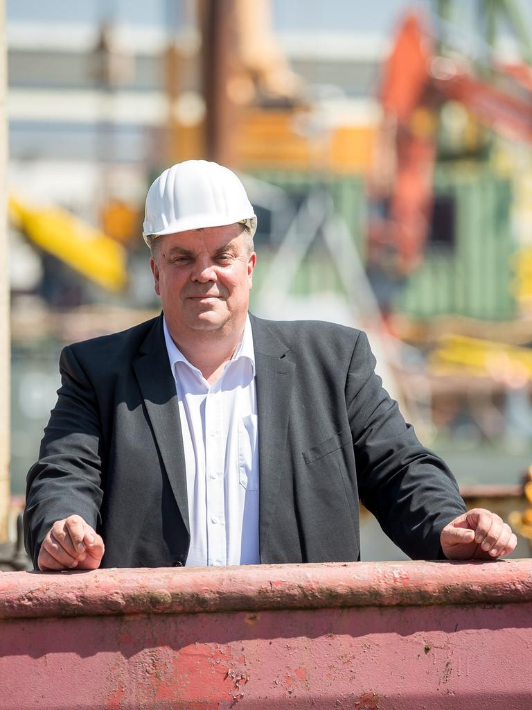 Carsten Feist, Oberbürgermeister der Stadt Wilhelmshaven steht mit Schutzhelm vor industrieller Hafenkulisse.