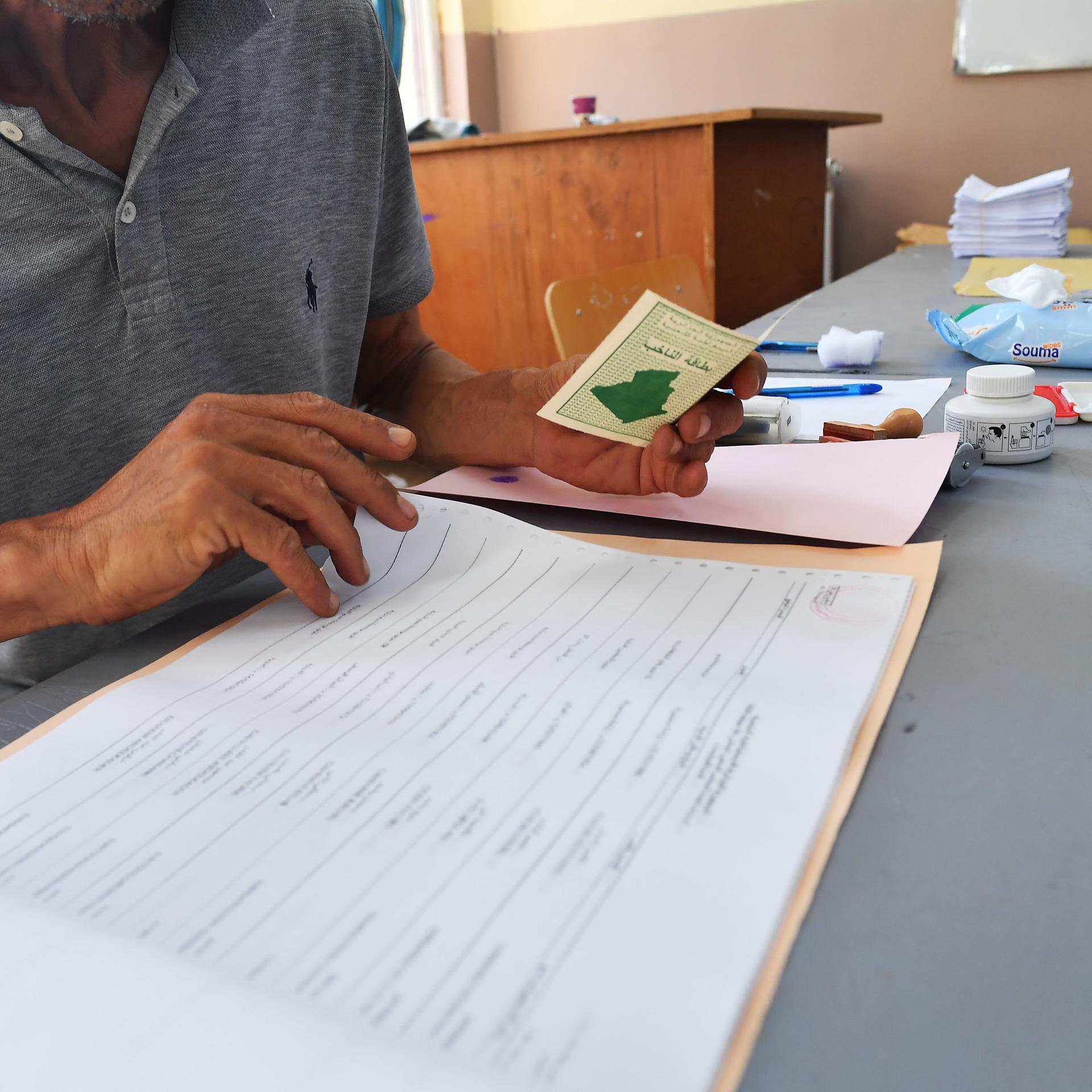 Ein Wahlhelfer überpüft einen Ausweis in einer Liste.