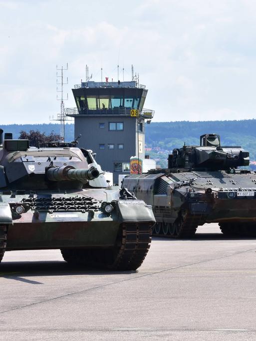 Panzer der Bundeswehr stehen nebeneinander geparkt auf einem Flugplatz. Dahinter sieht man den Tower. 