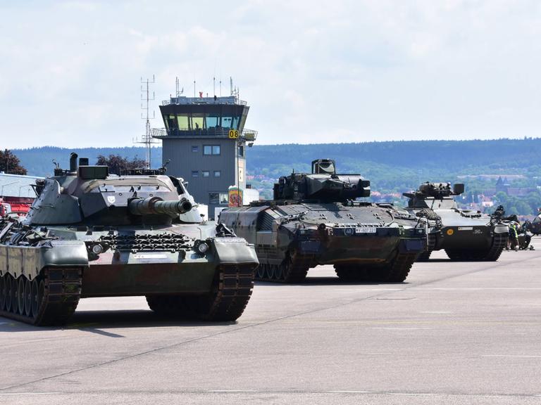 Panzer der Bundeswehr stehen nebeneinander geparkt auf einem Flugplatz. Dahinter sieht man den Tower. 