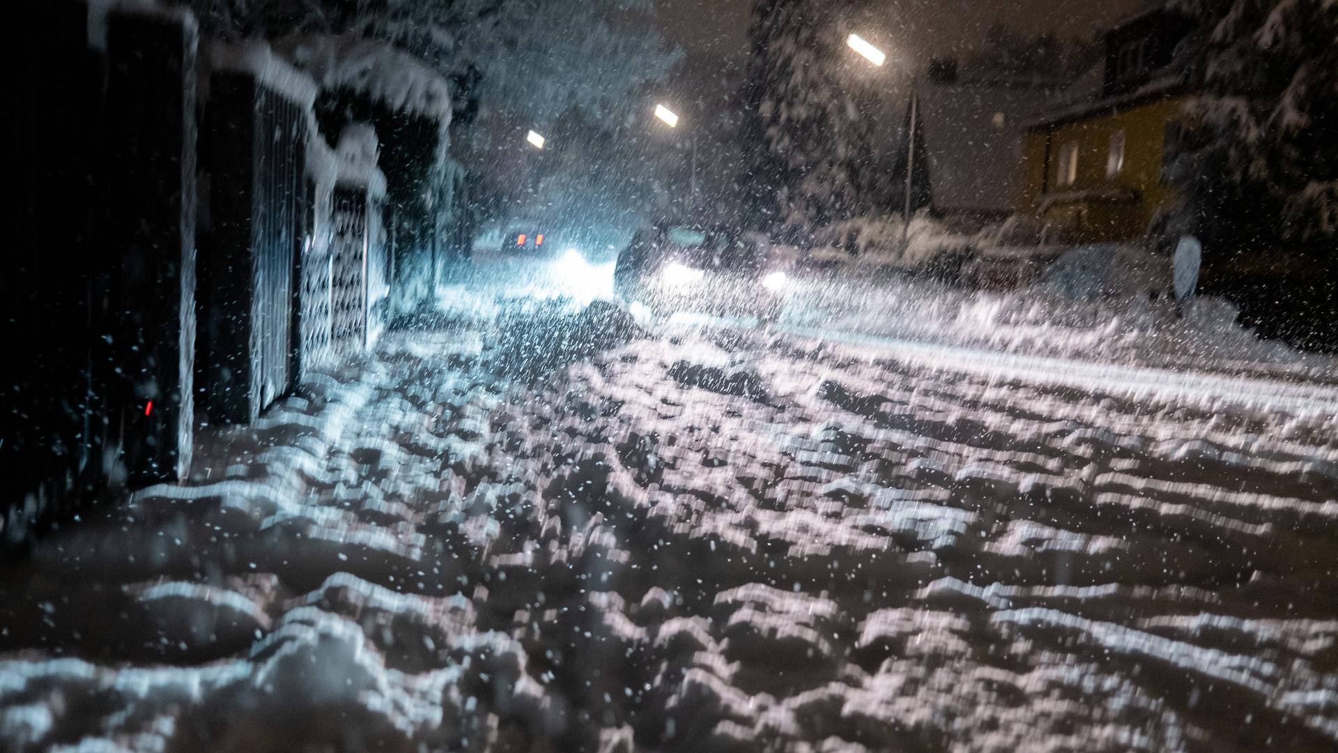 Das Foto zeigt eine schneebedeckte Straße. Im Hintergrund ist ein Auto.