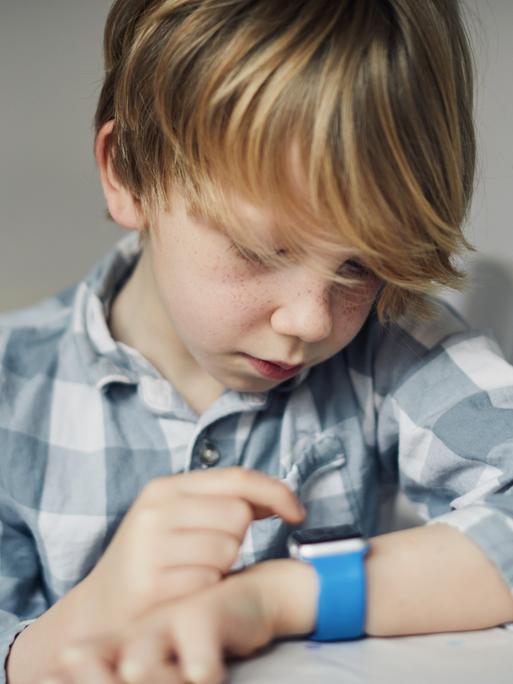 Ein Junge schaut auf sein Handgelenk wo er eine Smartwatch trägt.