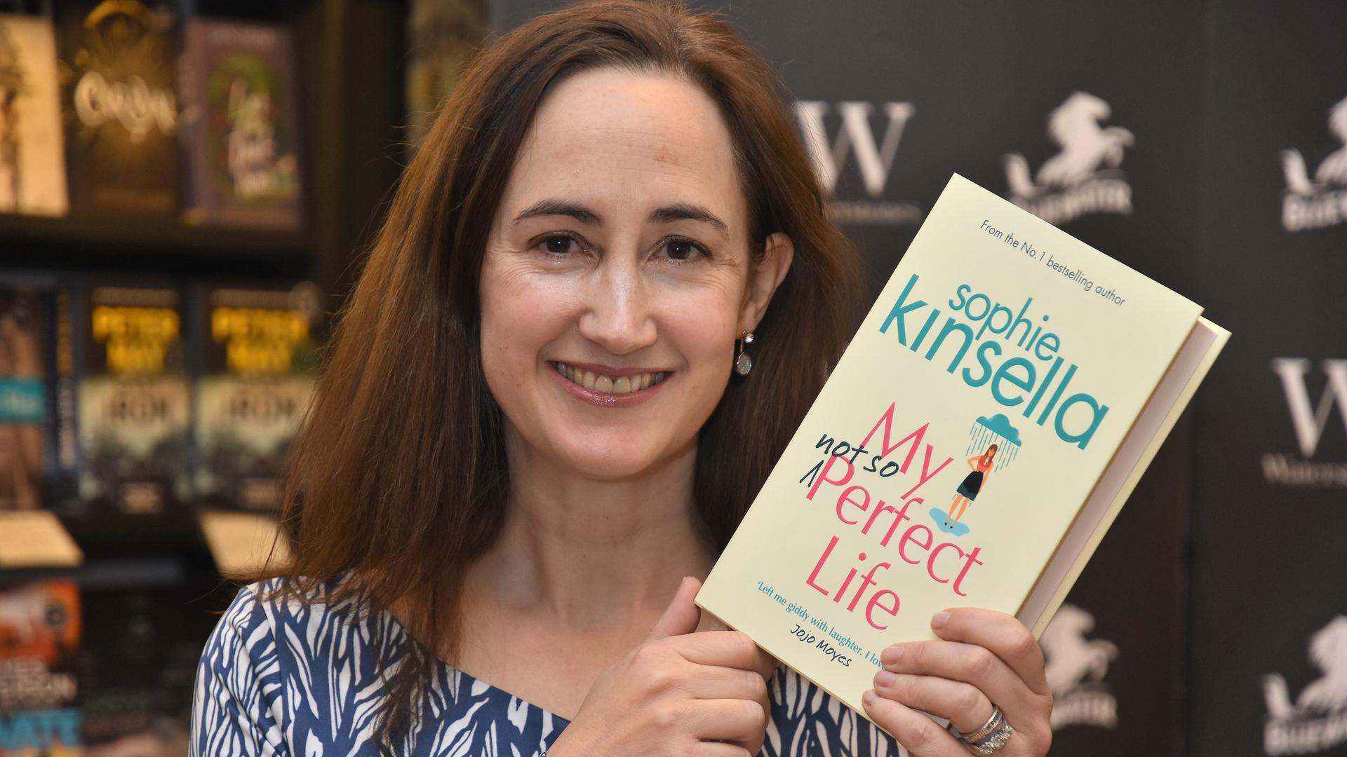 Die Autorin Sophie Kinsella hält ein Buch in die Hand und blickt in die Kamera. Die Autorin Sophie Kinsella hält ein Buch in die Hand und blickt in die Kamera.