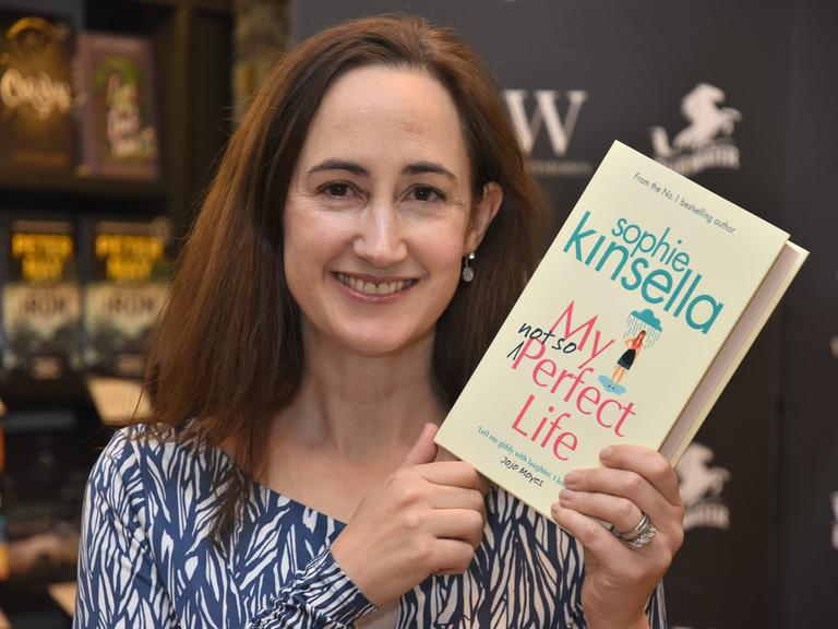 Die Autorin Sophie Kinsella hält ein Buch in die Hand und blickt in die Kamera.