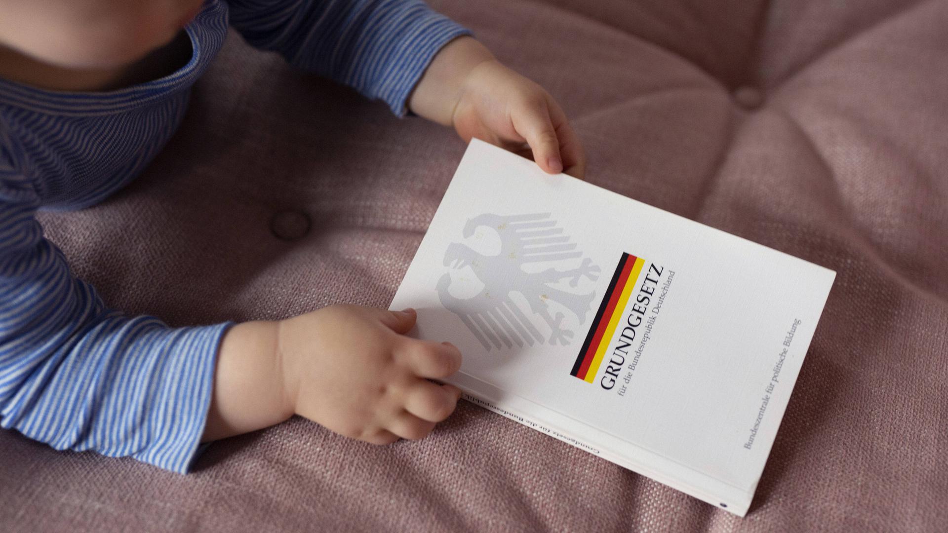 Ein Baby mit Grundgesetzbuch in den Händen.