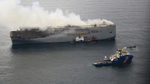 Mehrere kleinere Schiffe stehen neben dem brennenden Autofrachter.