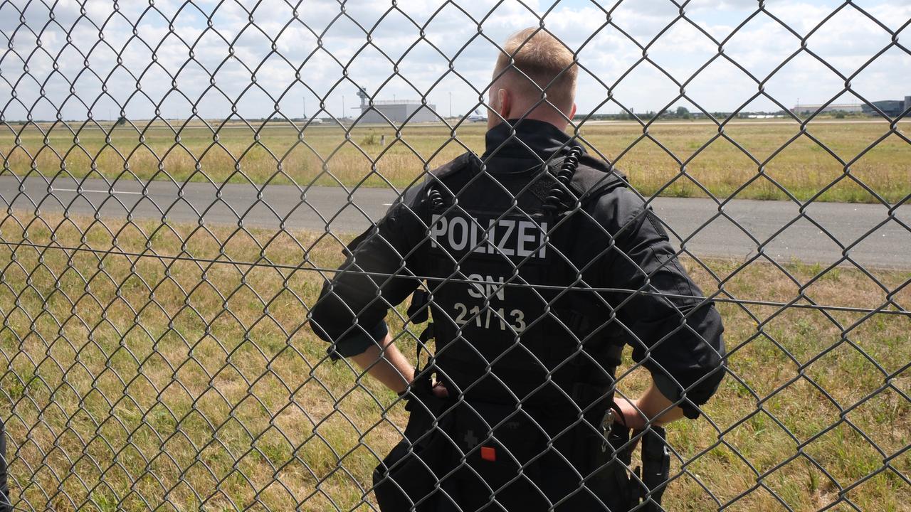 Ein Polizist steht auf dem Gelände des Flughafen-Leipzig/Halle hinter einem Gitter. Ein Polizist steht auf dem Gelände des Flughafen-Leipzig/Halle hinter einem Gitter.