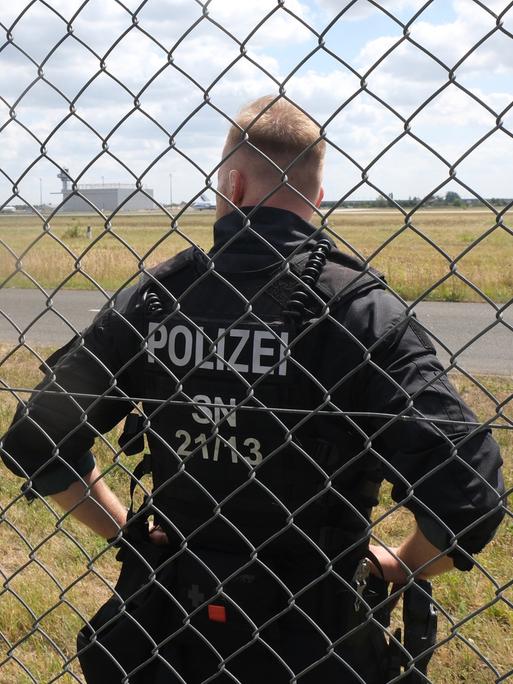 Ein Polizist steht auf dem Gelände des Flughafen-Leipzig/Halle hinter einem Gitter. 