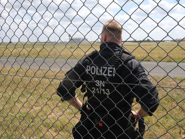 Ein Polizist steht auf dem Gelände des Flughafen-Leipzig/Halle hinter einem Gitter. 