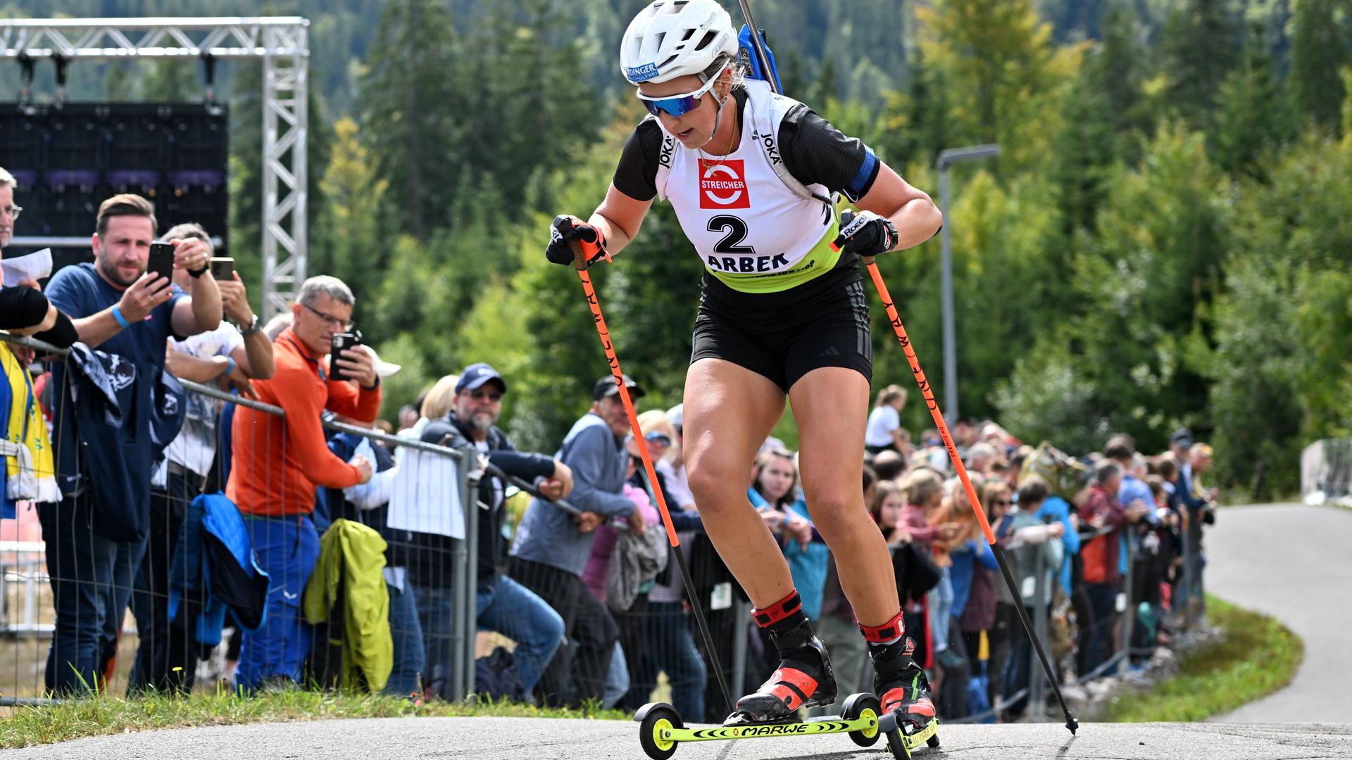 Franziska Preuss schiebt sich mit ihren Skirollern und Stecken den Berg hinauf, am Rand stehen viele Zuschauerinnen und Zuschauer