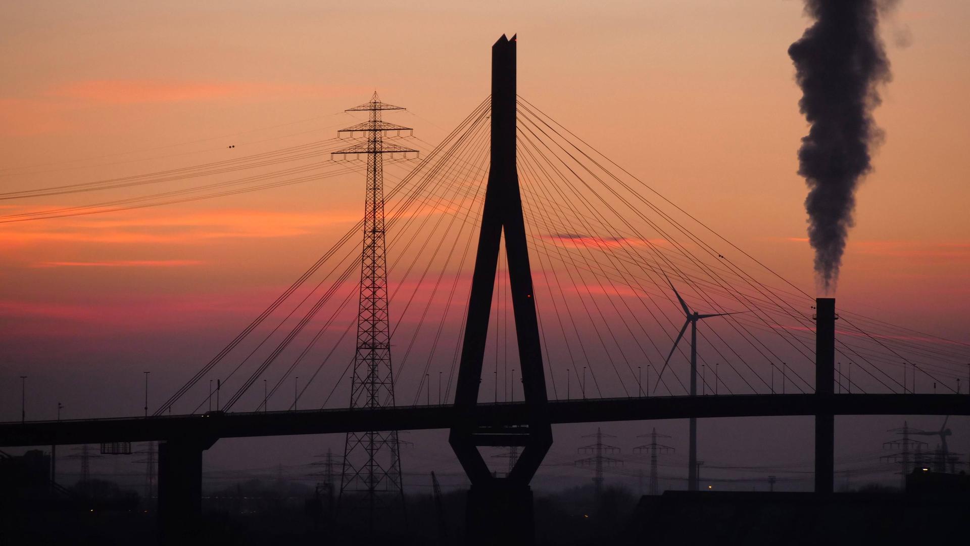 Die Köhbrandbrücke am Hamburger Hafen im Abendlicht. Ein Sonnenuntergang im Hintergrund und die Brücke erscheint wie ein Schattenbild davor. 