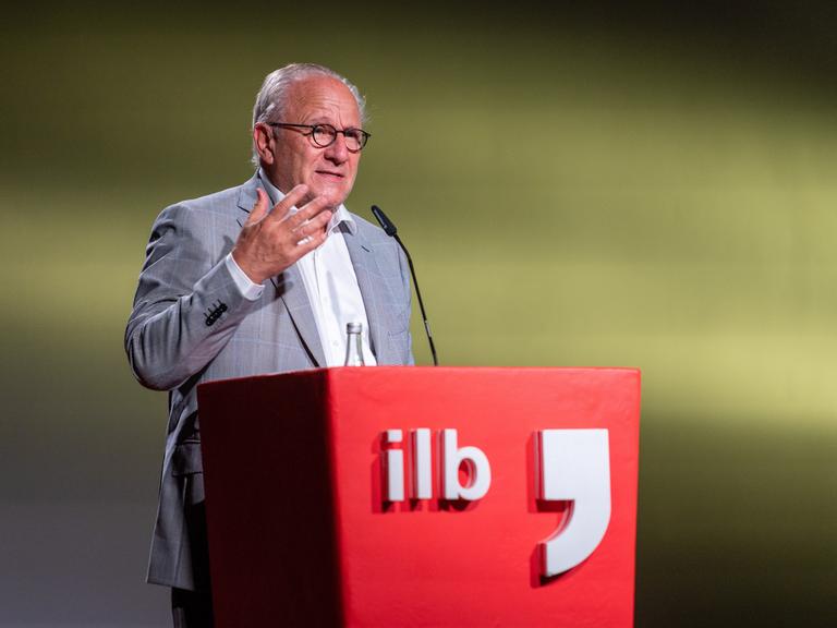 Ulrich Schreiber steht an einem roten Rednerpult mit der Aufschrift "ilb"