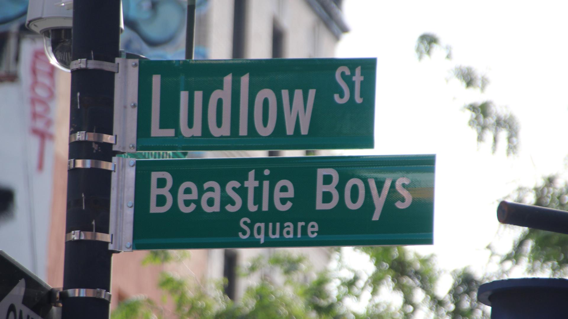 An einem Mast hängen zwei grüne Straßenschilder mit weißer Schrift: Ludlow Street und Beastie Boys Square.