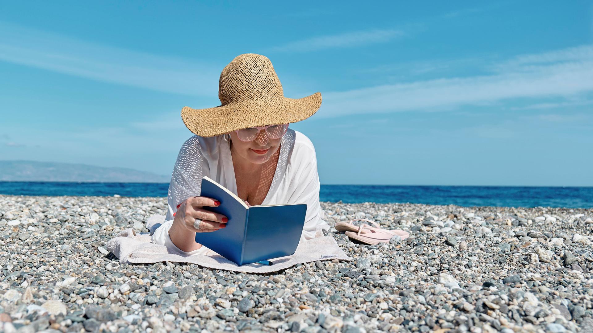 Eine Frau liest ein Buch an einem Strand