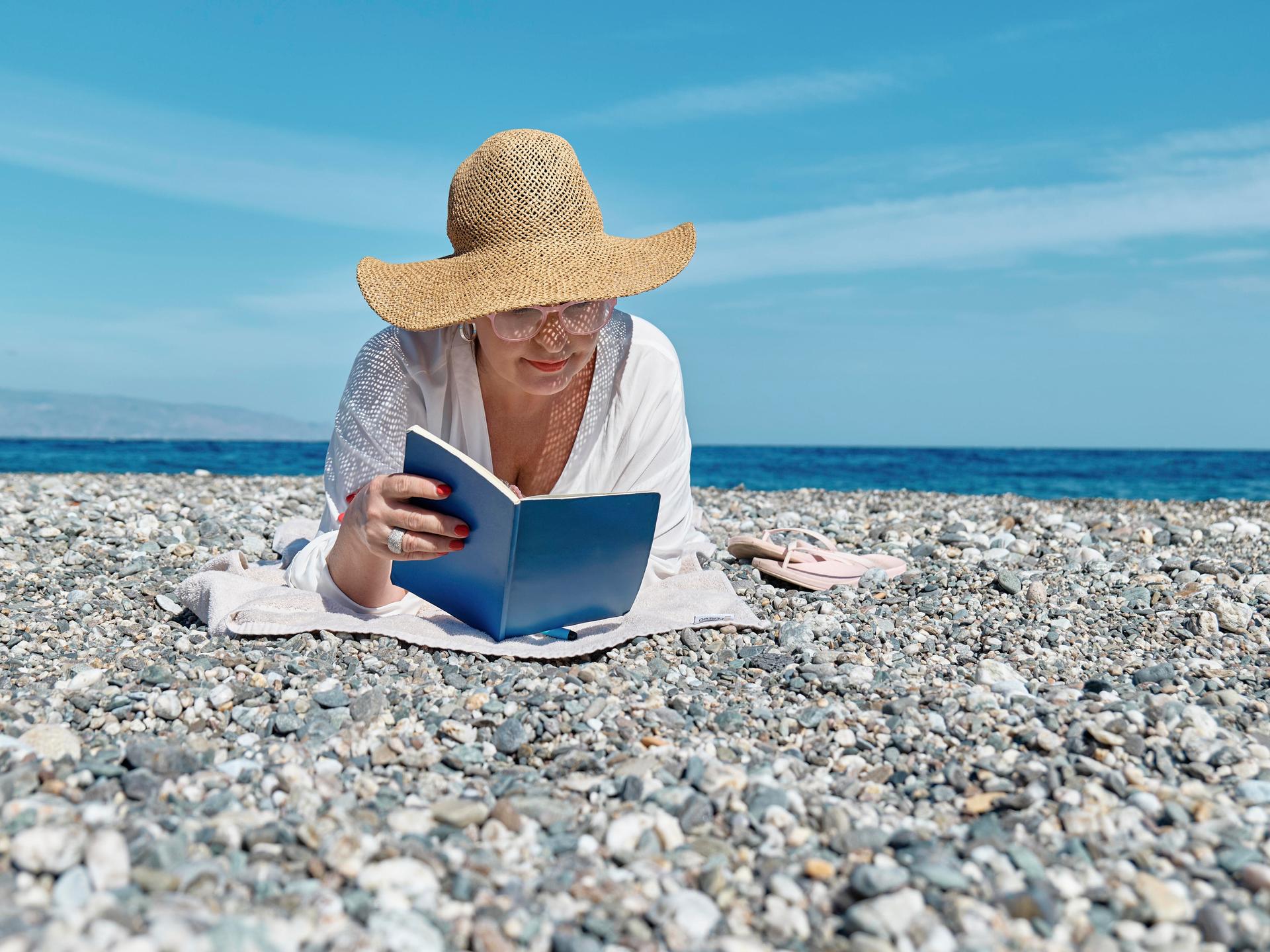 Eine Frau liest ein Buch an einem Strand