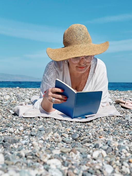 Eine Frau liest ein Buch an einem Strand