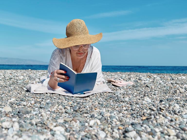 Eine Frau liest ein Buch an einem Strand