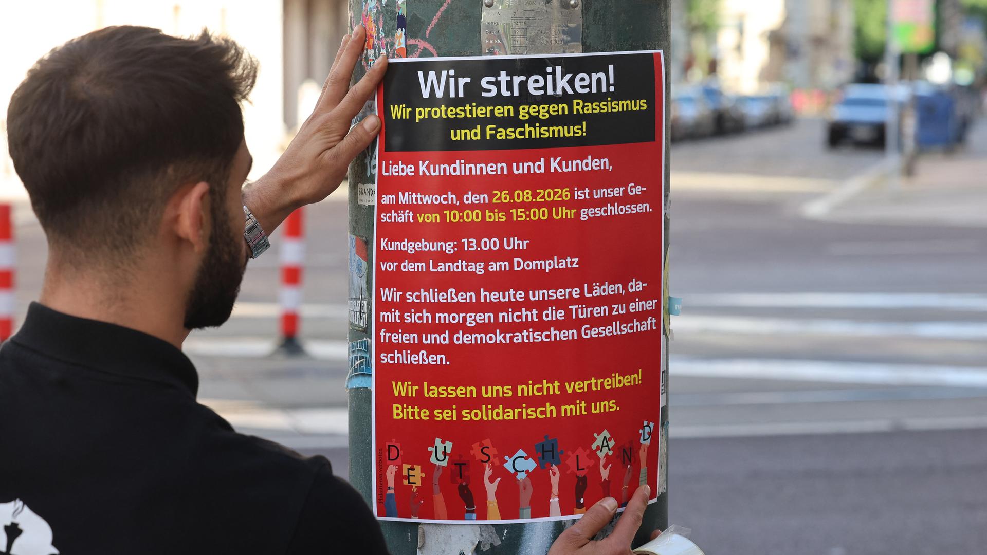 Ein Mann klebt ein Plakat für die Aktion an einen Laternen-Pfahl. Ein Mann klebt ein Plakat für die Aktion an einen Laternen-Pfahl.