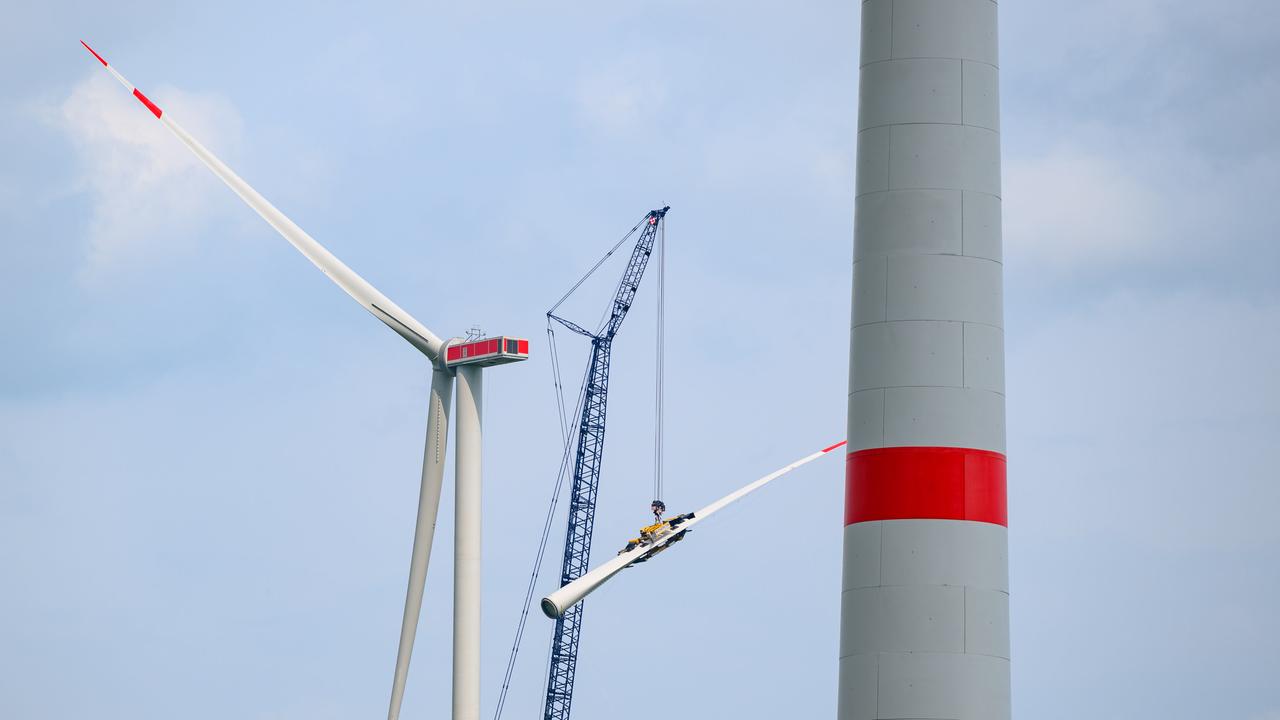 Zwei Windräder vor blauem Himmel, dazwischen steht ein Kran.