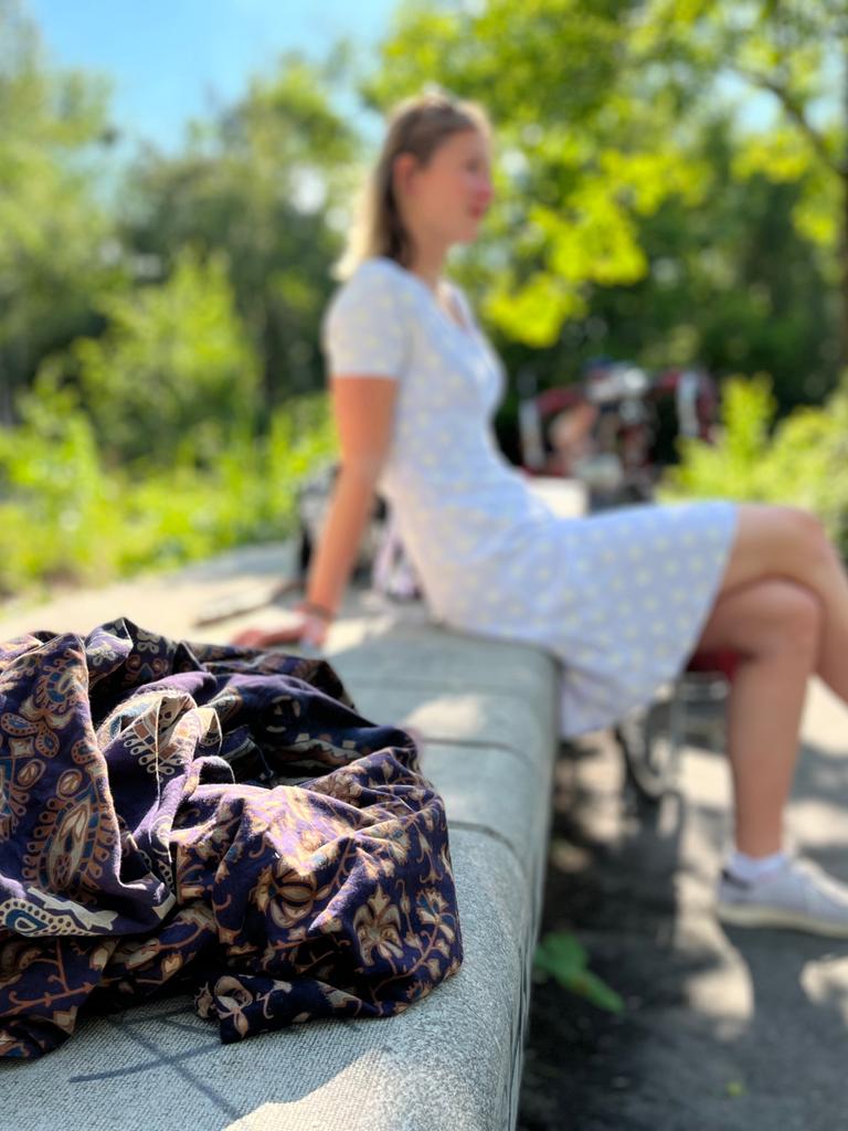 Die Studentin Nele sitzt in einem hellblauen Kleid auf einer Steinbank. Im Vordergrund liegt ihre Lieblingsdecke.