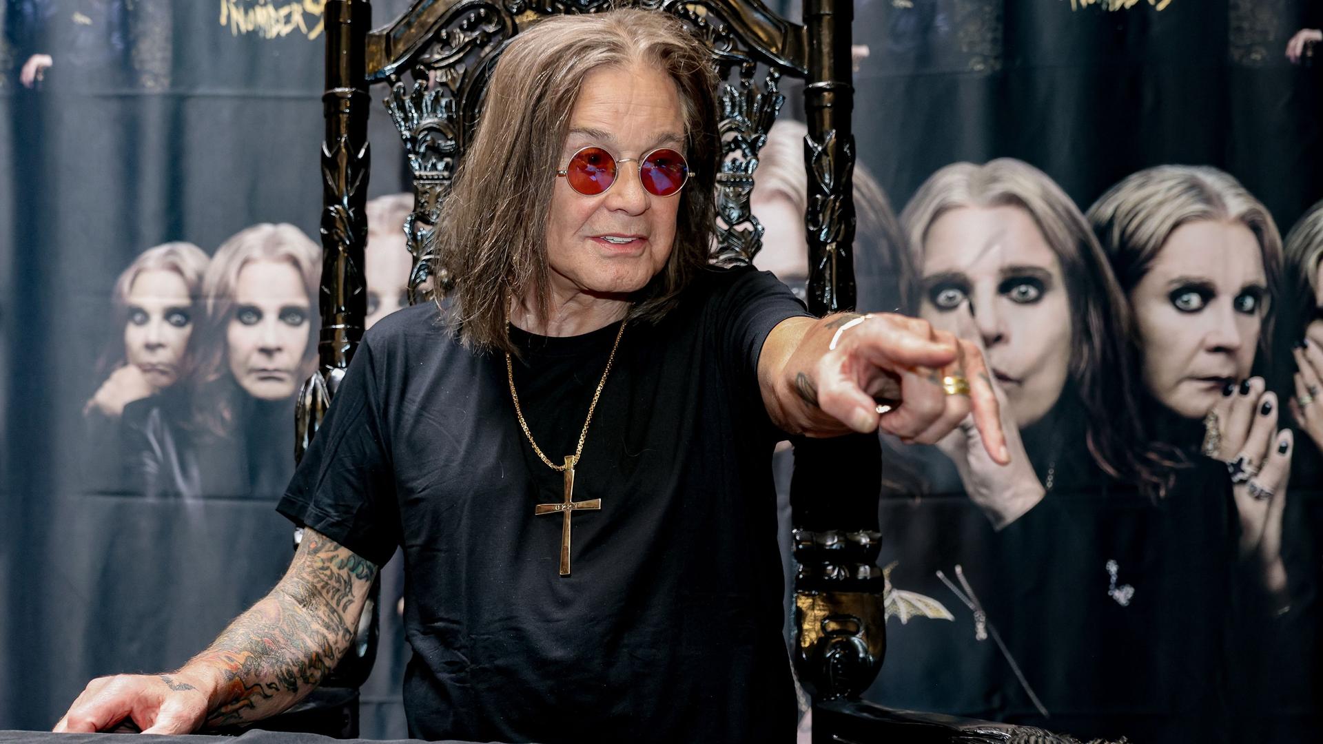 Der Heavy-Metal-Sänger Ozzy Osbourne bei einem Fototermin 2022: Er trägt ein schwarzes T-Shirt, Brille und eine goldene Halskette mit einem Kreuz.