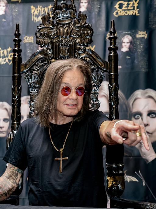 Der Heavy-Metal-Sänger Ozzy Osbourne bei einem Fototermin 2022: Er trägt ein schwarzes T-Shirt, Brille und eine goldene Halskette mit einem Kreuz.