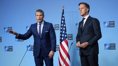 NATO-Generalsekretär Rutte und US-Verteidigungsminister Hegseth stehen beim Treffen der Verteidigungsminister in Brüssel nebeneinander auf der Bühne.