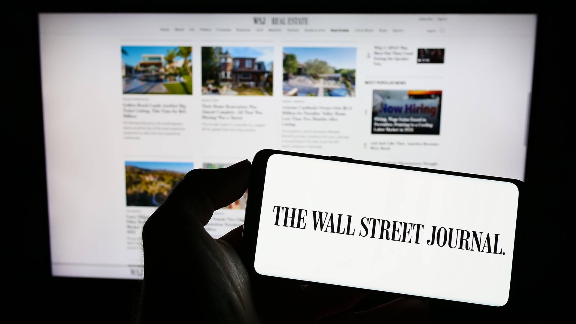 Das Logo des Wall Street Journal auf einem Handy-Bildschirm, im Hintergrund die Internetseite der Tageszeitung