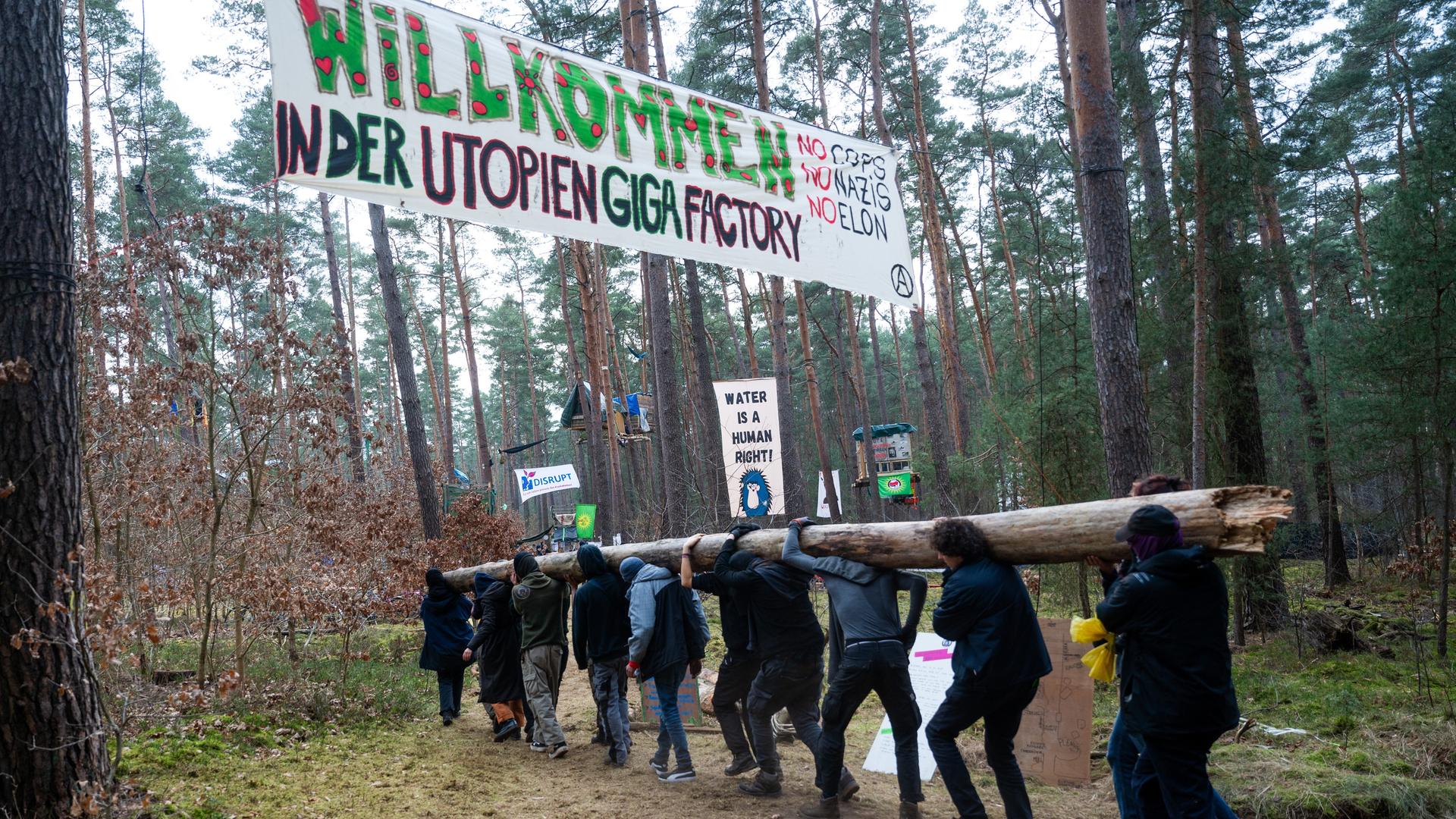 Aktivisten tragen in einem Protestcamp einen Baumstamm im Wald. Das Protestcamp richtet sich gegen eine geplante Erweiterung des Tesla-Werksgeländes in einem Waldgebiet nahe der Fabrik.