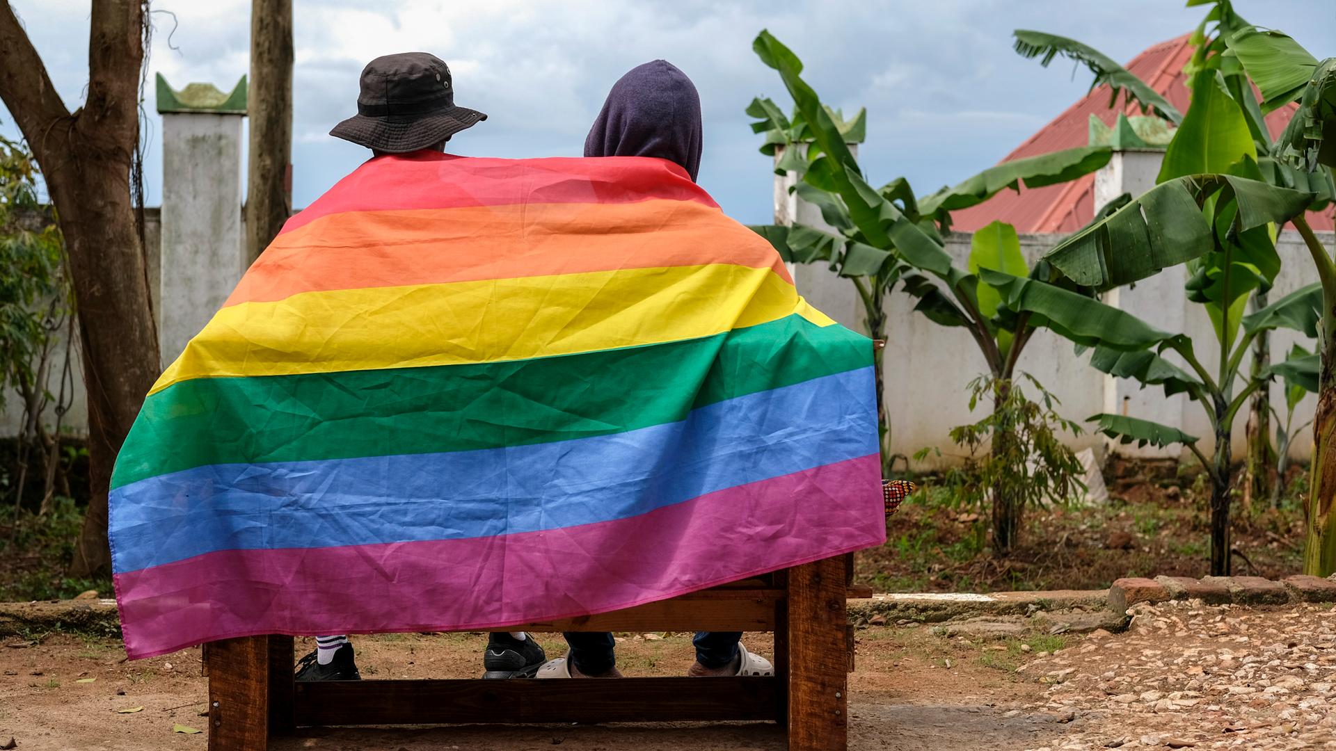 Ein schwules ugandisches Paar bedeckt sich mit einer Pride Flagge.