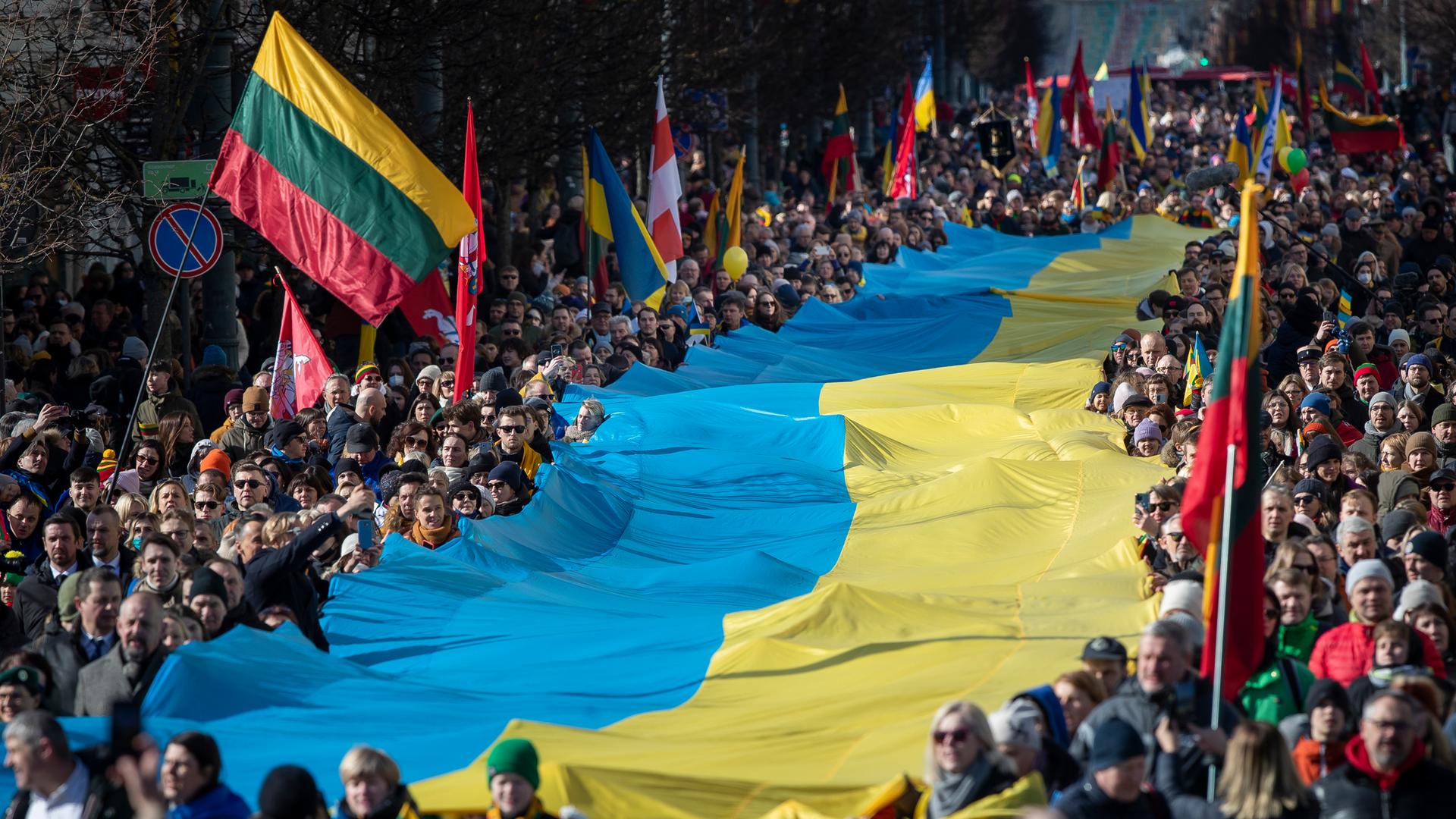Menschen tragen am 11.03.2022 eine riesige Ukrainische Flagge bei den Feierlichkeiten zu Litauens 1991 erlangter Unabhängigkeit in der Hauptstadt Vilnius