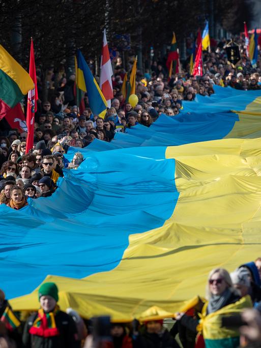 Menschen tragen am 11.03.2022 eine riesige Ukrainische Flagge bei den Feierlichkeiten zu Litauens 1991 erlangter Unabhängigkeit in der Hauptstadt Vilnius