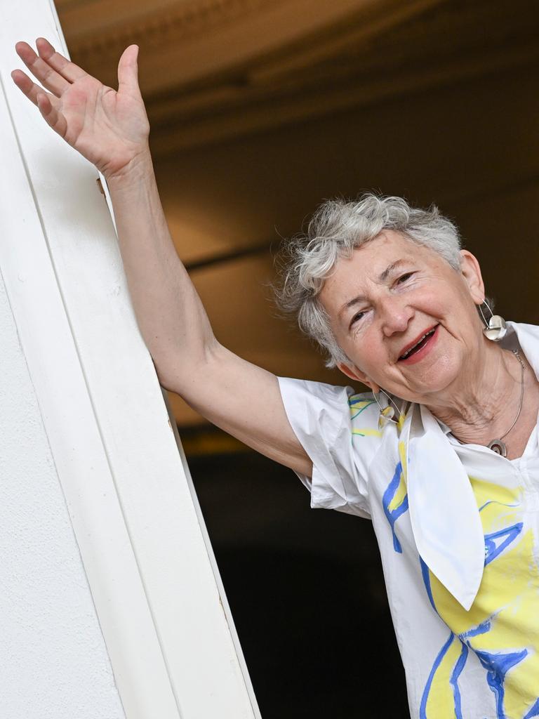 Die Künstlerin Gabriele Stötzer steht lachend an einem Türpfosten in ihrer Ausstellung „Dabei sein und nicht schweigen“ im Gropius Bau. Sie trägt eine weiße Jacke und nimmt eine lässige Pose ein. 