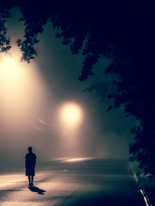 Eine Person ist allein nachts auf der Straße unterwegs.