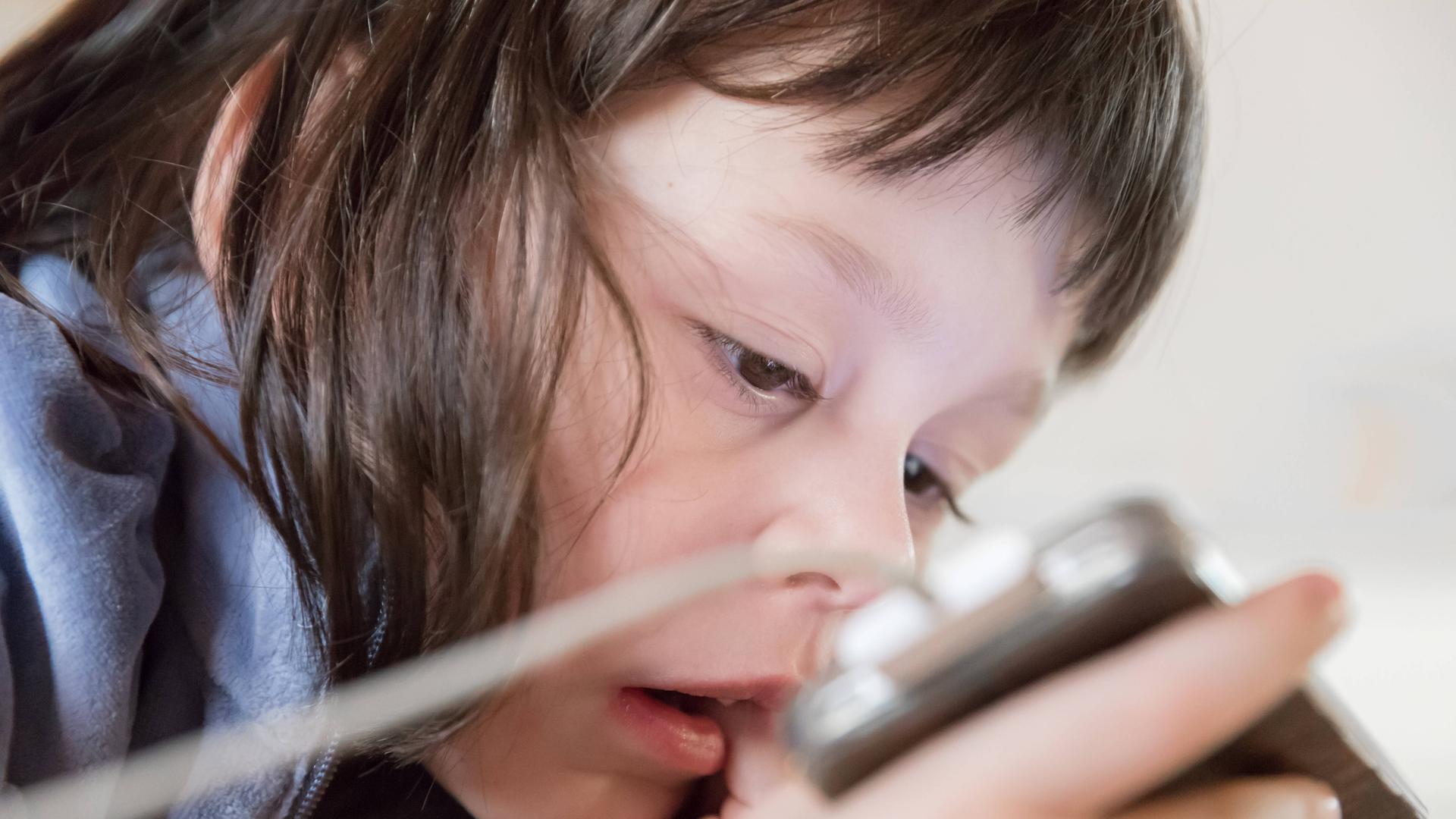 Ein Kind schaut gebannt auf den Bildschirm seines Smartphones.