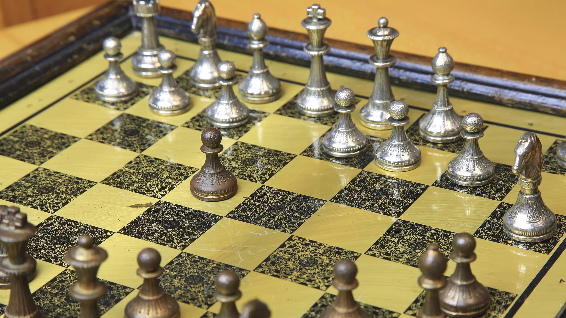 Ein edles Schachspiel auf einem gelb-schwarzen Brett mit metallischen Figuren in Silber und Bronze 