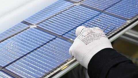 Eine Hand mit einem weißen Stoffhandschuh hebt ein Solarpanel in einer Fabrik an.