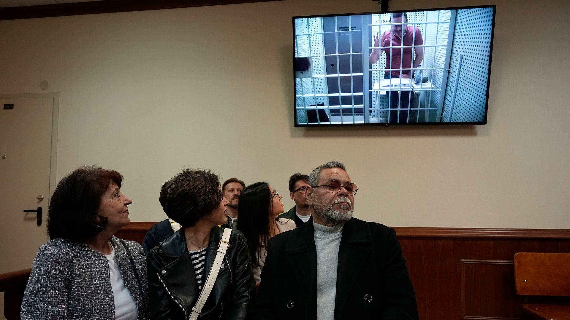 Mutter Tatjana (l) und Vater Waleri (r) des russischen Kremlkritikers Ilja Jaschin (Monitor) blicken auf einen Fernsehbildschirm, während er selbst per Video zu seinem Berufungsverfahren zugeschaltet ist