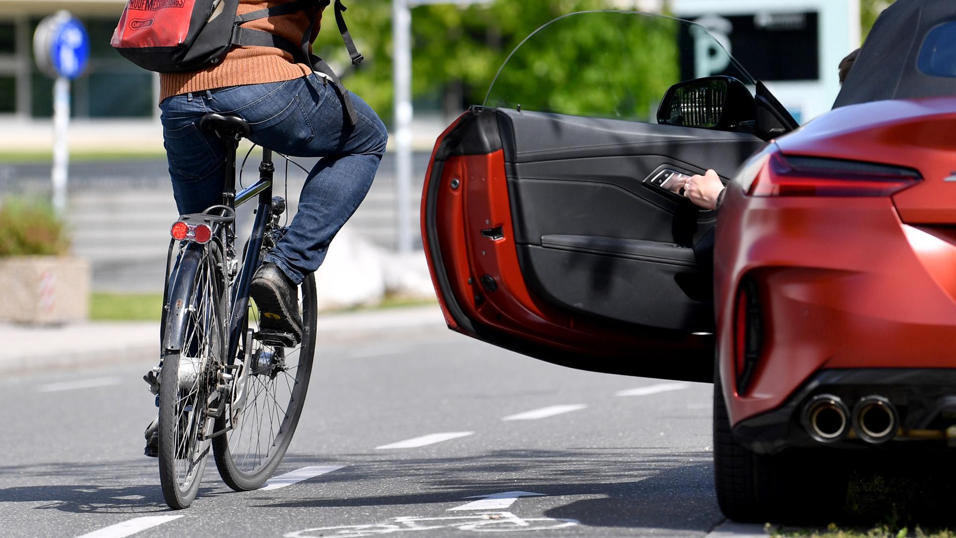 Ein Radfahrer fährt dicht an einer geöffneten Autotür vorbei.