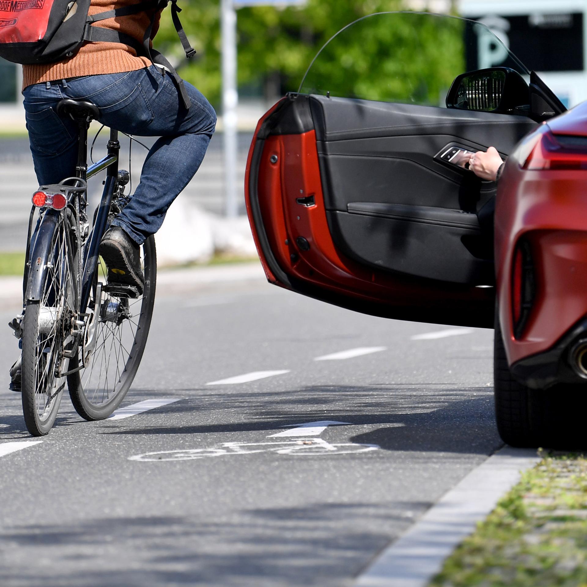 Ein Radfahrer fährt dicht an einer geöffneten Autotür vorbei.