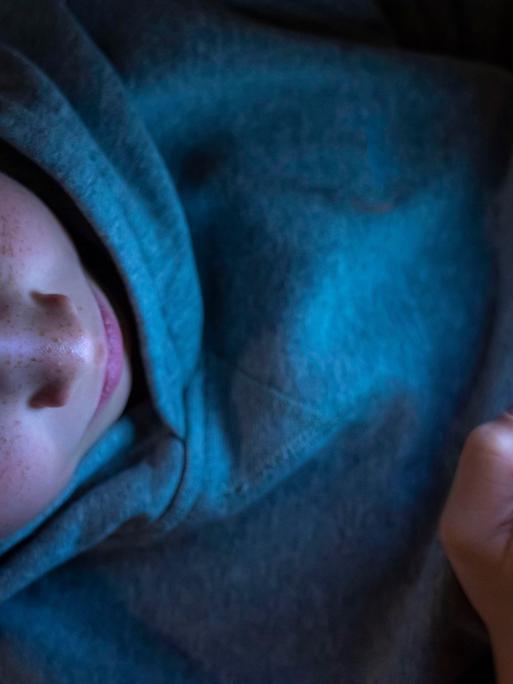 Ein 12-jähriges Kind hält ein Handy mit diversen Social-Media-Plattformen in der Hand