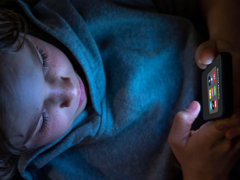 Ein 12-jähriges Kind hält ein Handy mit diversen Social-Media-Plattformen in der Hand