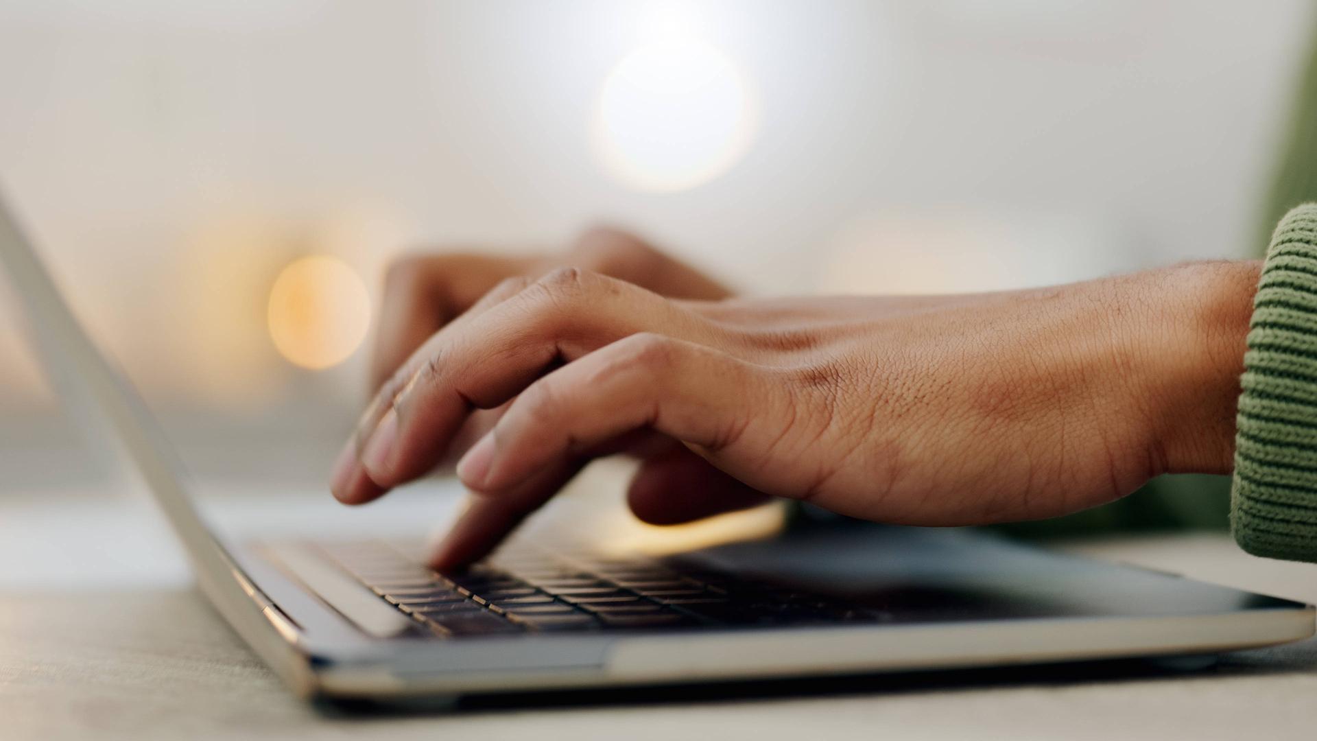 Hände, die auf einer Laptop-Tastatur einen Text eintippen.