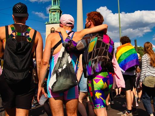 In einer Reihe stehen mehrere Demonstrierende beim CSD in Berlin in bunter Kleidung, eine Person legt einer anderen den Arm um die Schulter.