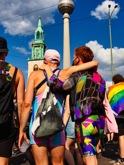In einer Reihe stehen mehrere Demonstrierende beim CSD in Berlin in bunter Kleidung, eine Person legt einer anderen den Arm um die Schulter.