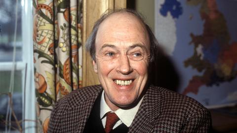 Roald Dahl trägt ein kariertes Jacket und lacht in die Kamera.