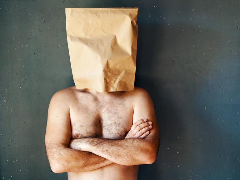 Ein Mann mit freiem Oberkörper hat eine Papiertüte über den Kopf gestülpt. Seine Arme sind verschränkt. Ein Mann mit freiem Oberkörper hat eine Papiertüte über den Kopf gestülpt. Seine Arme sind verschränkt.