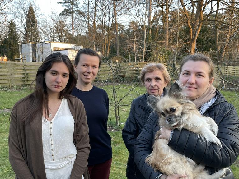Das Bild zeigt vier Frauen, die auf einer Wiese stehen. Eine hält einen kleinen Hund auf dem Arm.