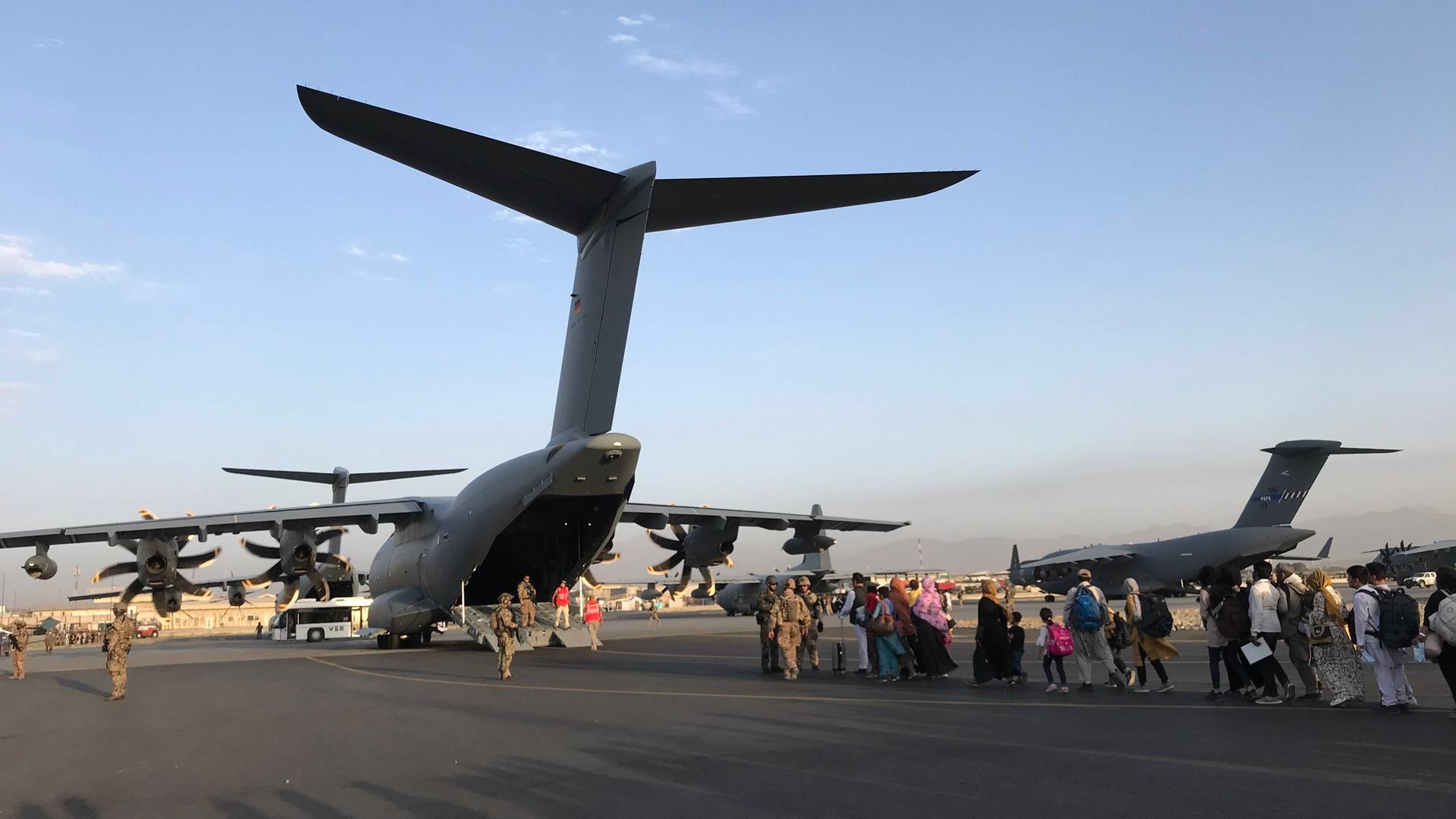 Menschen auf dem Rollfeld des Flughafens in Kabul drängen sich hinter einem Flugzeug der Bundeswehr Menschen auf dem Rollfeld des Flughafens in Kabul drängen sich hinter einem Flugzeug der Bundeswehr