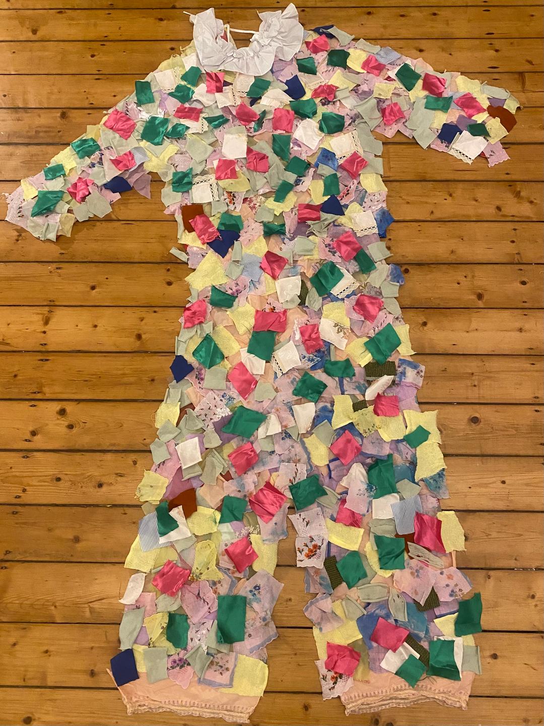 Ein großes Clownskostüm aus bunten Flicken liegt auf einem Dielenboden ausgebreitet
